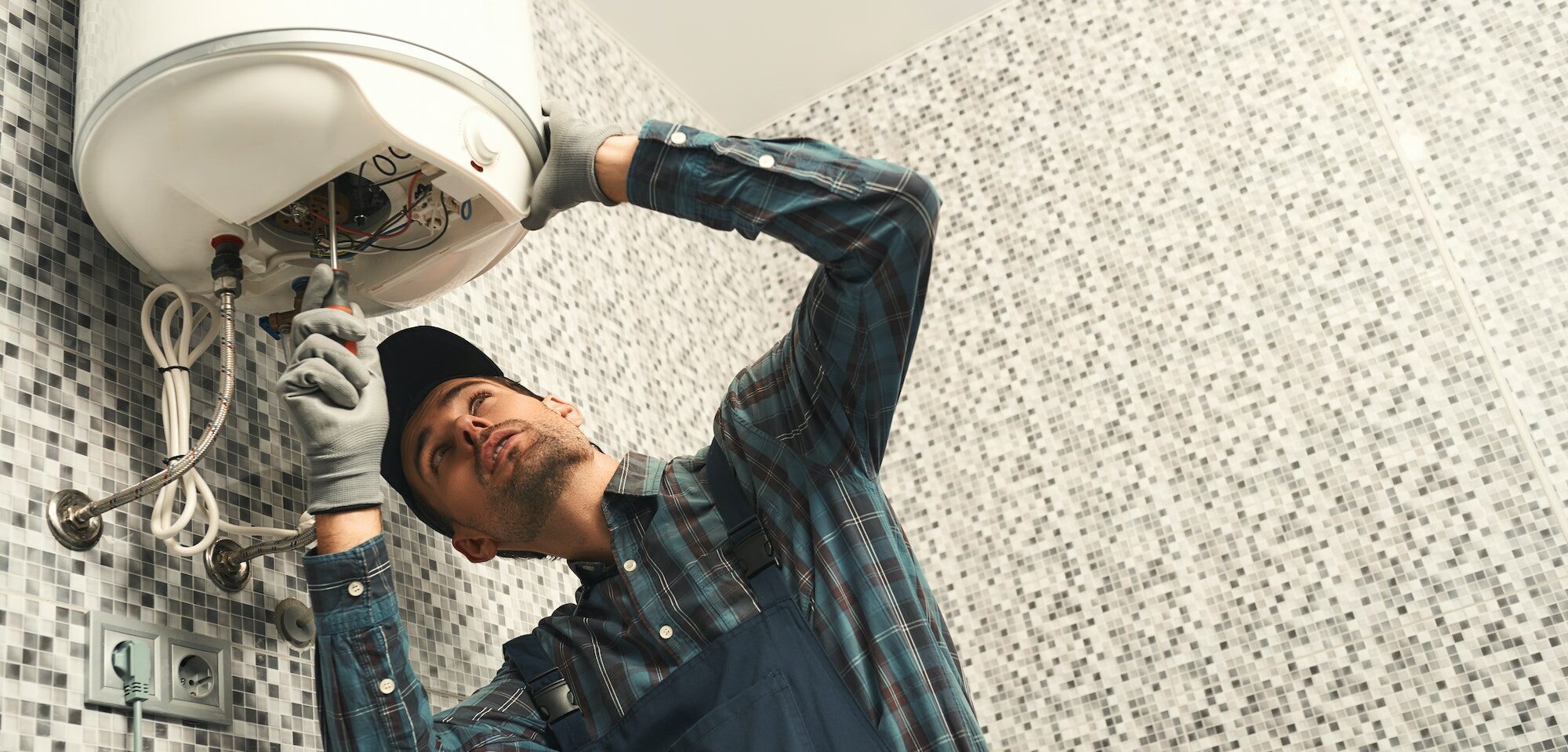 Plumber installing electric heating boiler. Young handyman in uniform setting up electric heating